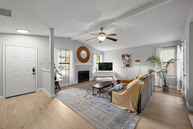 Living room with cathedral ceiling featuring light engineered wood flooring, ceiling fan, a tiled wood-burning fireplace. | Image 4