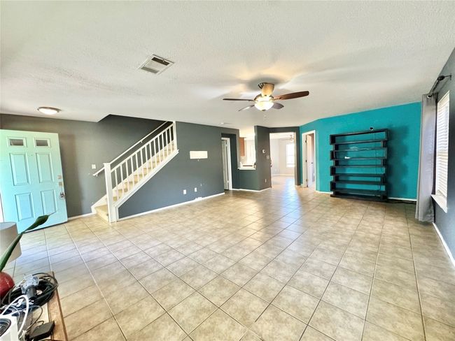 Unfurnished living room with a textured ceiling, stairs, ceiling fan, and tile patterned floors | Image 4