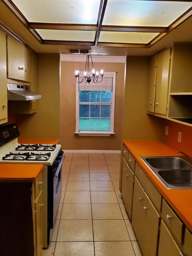Kitchen with black range with gas cooktop, under cabinet range hood, a sink, a chandelier, and light tile patterned floors | Image 16