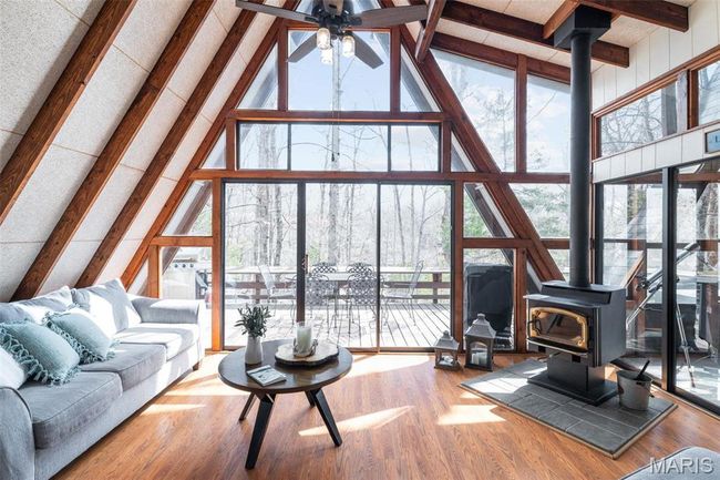 Living area featuring a wall of windows, a wood stove, wood finished floors, and beam ceiling | Image 5