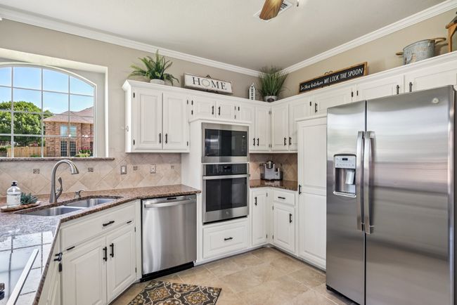 Kitchen with stainless steel appliances, white cabinetry, tasteful backsplash, stone counters, and light tile patterned floors | Image 15