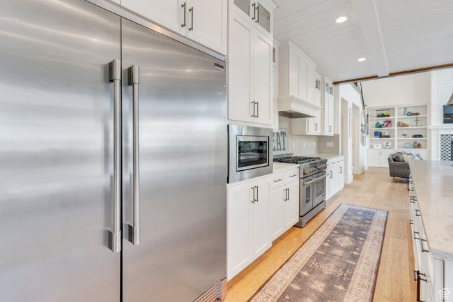 Kitchen with built in appliances, beamed ceiling, white cabinets, glass insert cabinets, and light wood-style flooring | Image 21