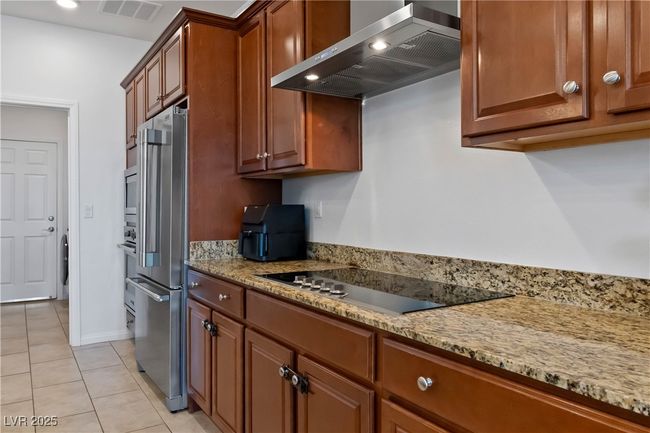 Kitchen with visible vents, high quality fridge, black electric stovetop, wall chimney range hood, and light tile patterned flooring | Image 20