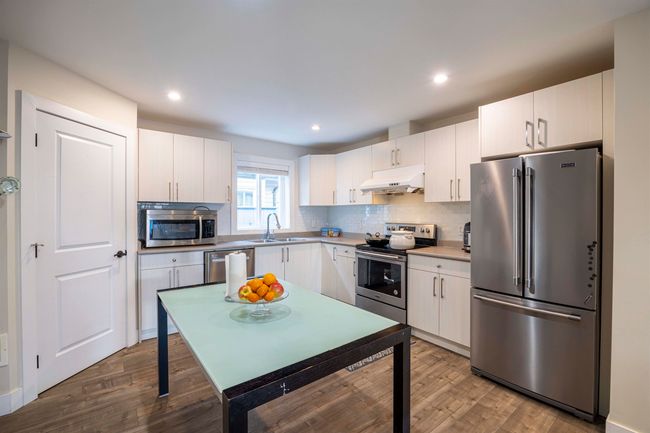 Kitchen with under cabinet range hood, a sink, appliances with stainless steel finishes, decorative backsplash, and dark wood-style flooring | Image 9