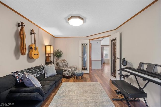 Den with crown molding, wood finished floors, and a textured ceiling | Image 6