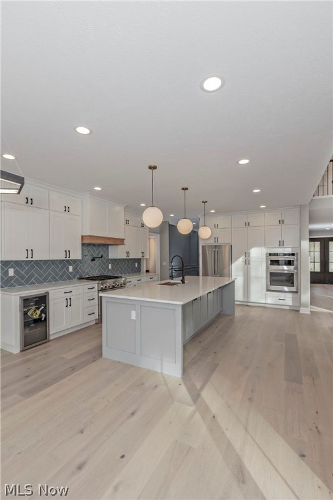Kitchen featuring light hardwood / wood-style floors, premium appliances, an island with sink, sink, and tasteful backsplash | Image 24