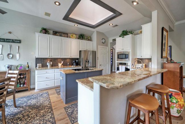 Kitchen featuring tasteful backsplash, appliances with stainless steel finishes, white cabinets, a center island, and a peninsula | Image 12