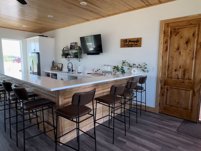 Bar featuring wooden ceiling, dark wood-type flooring, a sink, baseboards, and stainless steel fridge | Image 25
