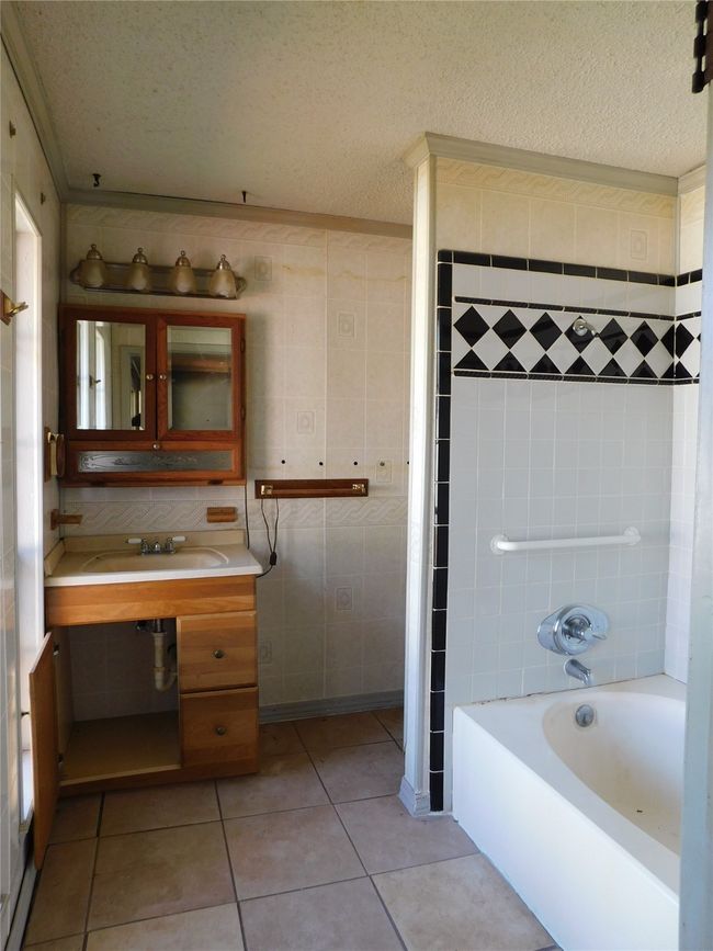 Bathroom with tile patterned floors, tile walls, shower / tub combination, and a textured ceiling | Image 18