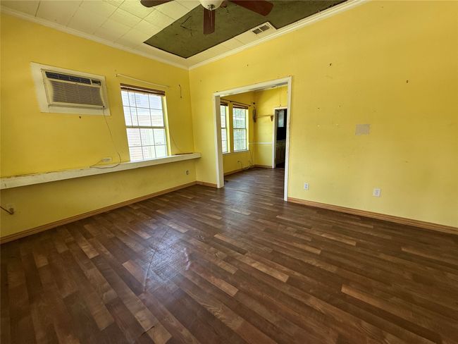 Empty room with ornamental molding, dark wood-style floors, a ceiling fan, baseboards, and an AC wall unit | Image 6
