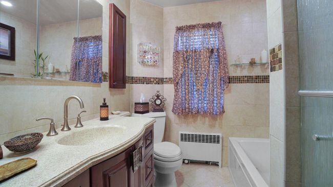 Full bathroom with a tub, radiator heating unit, tile walls, and tile patterned flooring | Image 10