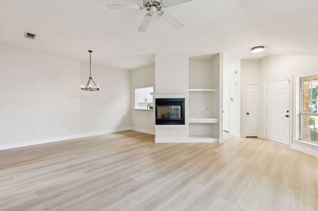 Unfurnished living room featuring light wood-style floors, a multi sided fireplace, ceiling fan, vaulted ceiling, and a chandelier | Image 8