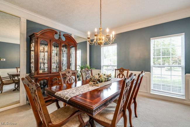 Dining room featuring ornamental molding, light colored carpet, a chandelier, wainscoting, and a decorative wall | Image 13