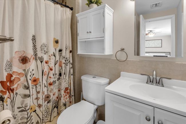 Bathroom featuring visible vents, curtained shower, toilet, vanity, and tile walls | Image 7