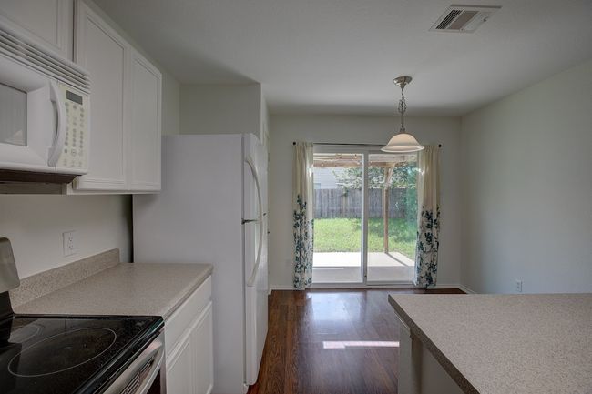 Kitchen featuring white appliances, dark wood-style flooring, white cabinetry, light countertops, and hanging light fixtures | Image 22