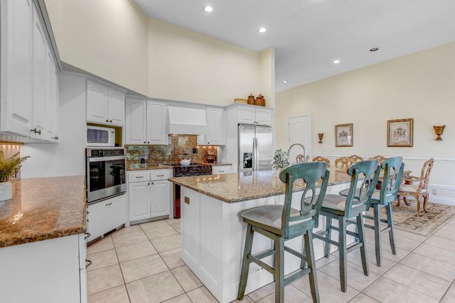 Kitchen featuring light tile patterned floors, dark stone countertops, stainless steel appliances, a kitchen bar, and a high ceiling | Image 18
