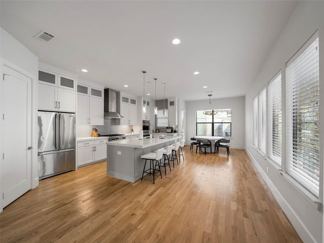 Kitchen with stainless steel appliances, wall chimney range hood, light wood-style floors, a kitchen island with sink, and recessed lighting | Image 12