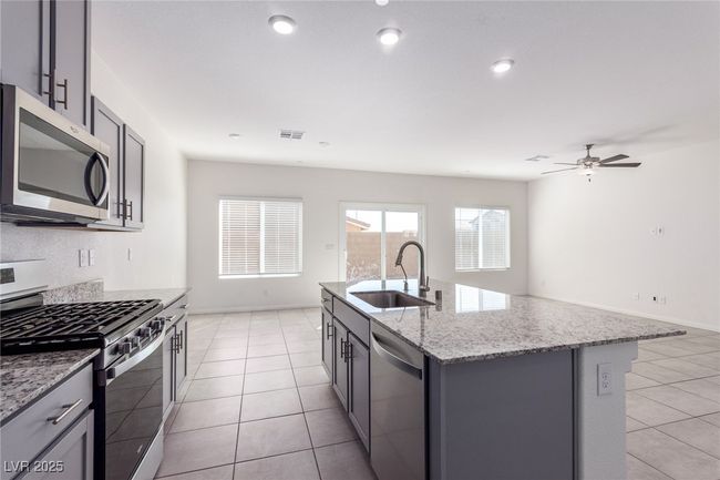 Kitchen featuring light tile patterned flooring, light stone countertops, visible vents, appliances with stainless steel finishes, and a sink | Image 8