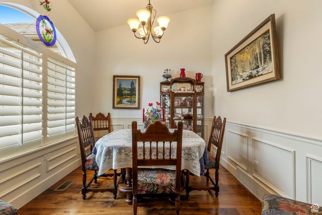 Dining space featuring a chandelier, a decorative wall, a wainscoted wall, wood finished floors, and vaulted ceiling | Image 11