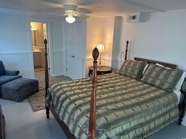 Bedroom featuring wainscoting, finished concrete floors, ensuite bathroom, and ceiling fan | Image 18
