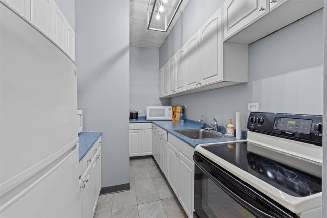Kitchen with white appliances, a sink, white cabinets, light tile patterned floors, and dark countertops | Image 16