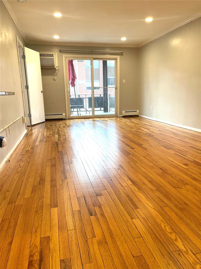 Empty room with a wall mounted air conditioner, ornamental molding, baseboard heating, and wood-type flooring | Image 6