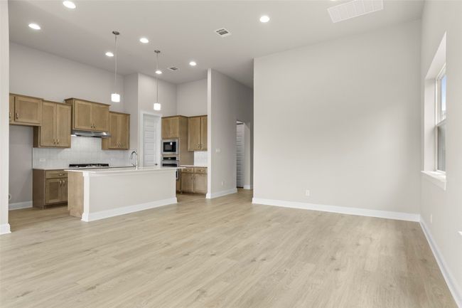 Kitchen featuring under cabinet range hood, brown cabinetry, light wood finished floors, decorative backsplash, and open floor plan | Image 14