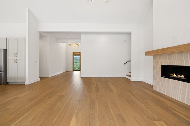 Unfurnished living room featuring light wood-type flooring, stairway, a fireplace, a chandelier, and baseboards | Image 5