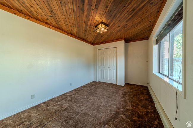 Unfurnished bedroom with carpet flooring, baseboards, a closet, wood ceiling, and ornamental molding | Image 13