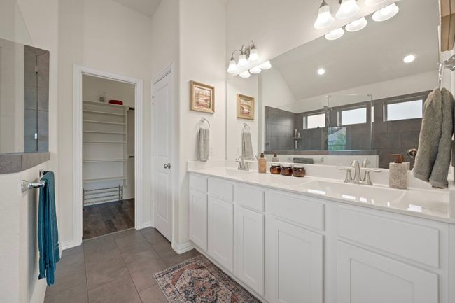 Bathroom featuring double vanity, tiled shower, a walk in closet, lofted ceiling, and tile patterned flooring | Image 14