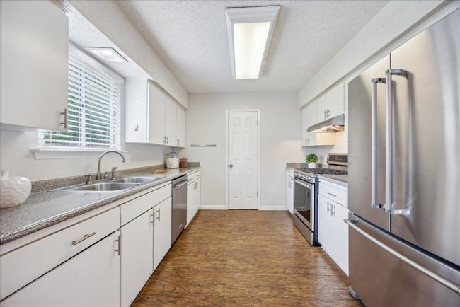 Kitchen with appliances with stainless steel finishes, white cabinets, dark wood-style floors, under cabinet range hood, and a textured ceiling | Image 10