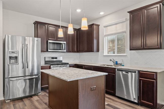 Kitchen featuring a center island, sink, decorative light fixtures, laminate / wood-style flooring, and stainless steel appliances (fridge to be removed) | Image 15