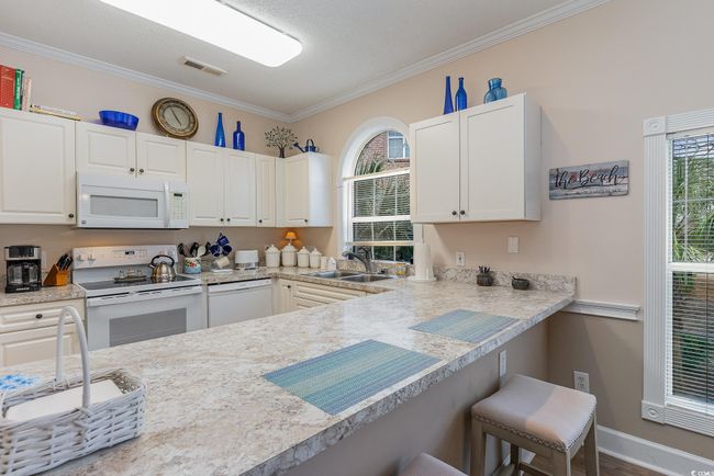 Kitchen with a kitchen bar, light stone countertops, white appliances, sink, and white cabinets | Image 7