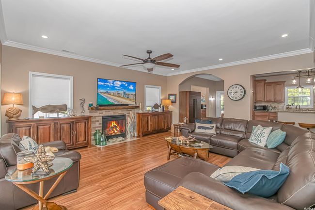 Living area with light wood-style floors, arched walkways, a ceiling fan, a fireplace, and recessed lighting | Image 14