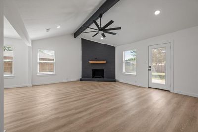 Unfurnished living room with ceiling fan, vaulted ceiling with beams, light wood-type flooring, and a brick fireplace | Image 2