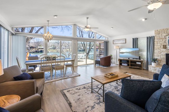 Living room with ceiling fan with notable chandelier, a stone fireplace, wood finished floors, and high vaulted ceiling | Image 7