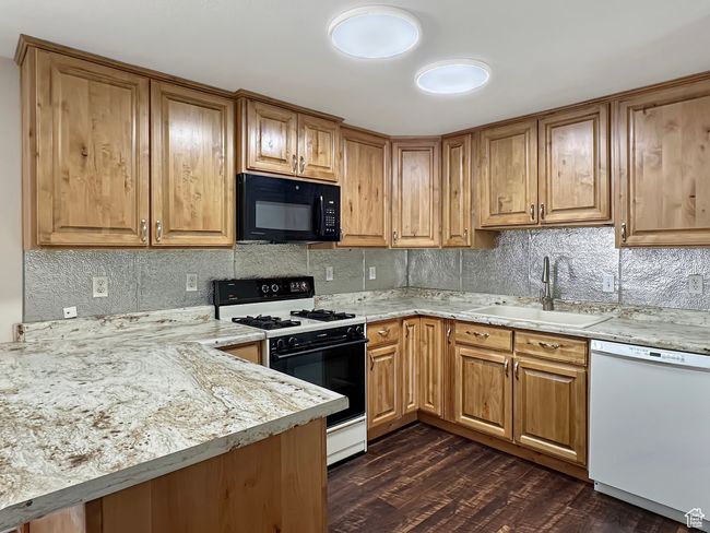 Kitchen with black microwave, white dishwasher, range with gas stovetop, a sink, and decorative backsplash | Image 5