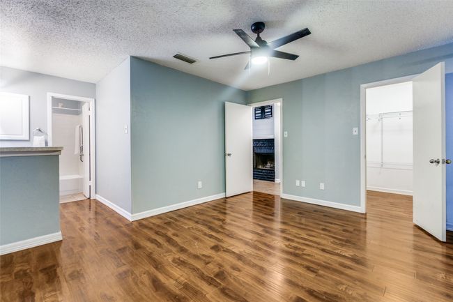 Unfurnished bedroom with a textured ceiling, wood finished floors, a fireplace, a walk in closet, and ceiling fan | Image 15