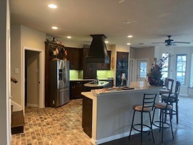Kitchen with dark brown cabinets, recessed lighting, custom exhaust hood, stainless steel fridge, and a spacious island | Image 11