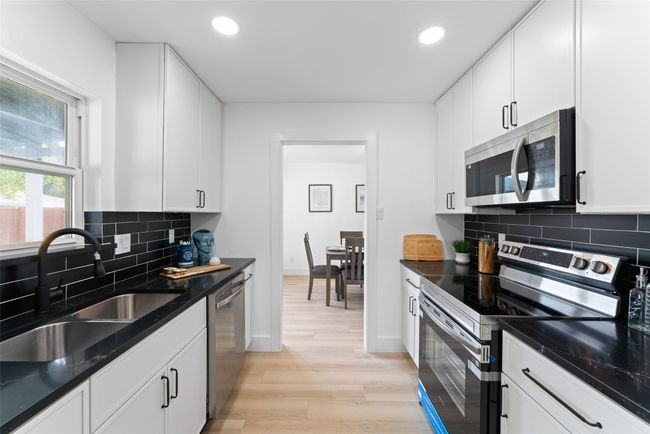 Kitchen featuring appliances with stainless steel finishes, light wood-type flooring, recessed lighting, tasteful backsplash, and white cabinets | Image 8