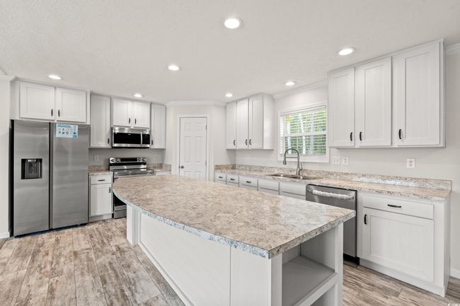 Kitchen featuring light countertops, a center island, appliances with stainless steel finishes, and a sink | Image 10