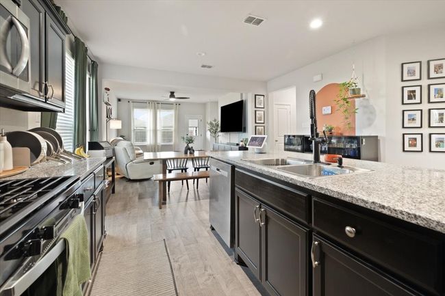 Kitchen with stainless steel appliances, gas stove top, open floor plan feeds into the dining area, light ceramic tile floors, and a ceiling fan in the living room | Image 15