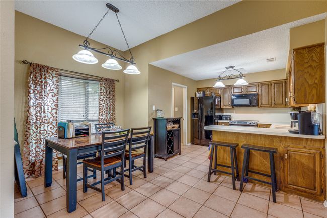 Kitchen with black appliances, a peninsula, brown cabinetry, light countertops, and light tile patterned flooring | Image 7