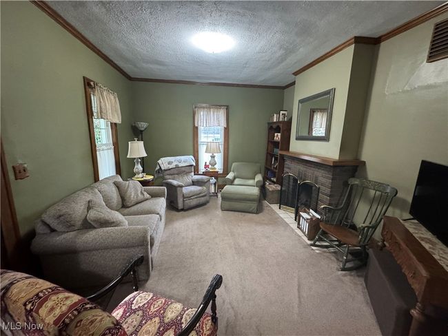 Carpeted living room featuring crown molding, a textured ceiling, and a brick fireplace | Image 5