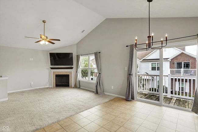 unfurnished living room with carpet flooring, high vaulted ceiling, a chandelier, a fireplace, and ceiling fan | Image 19