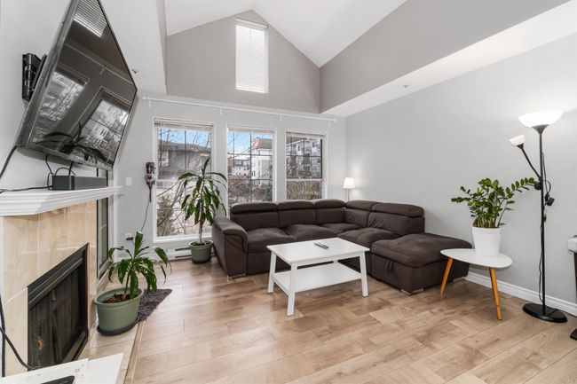 Living area featuring light wood finished floors, a tile fireplace, high vaulted ceiling, and baseboards | Image 7