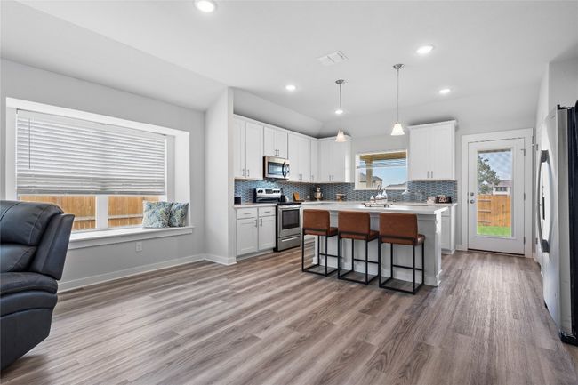 Kitchen featuring appliances with stainless steel finishes, open floor plan, a kitchen bar, light countertops, and white cabinetry | Image 16