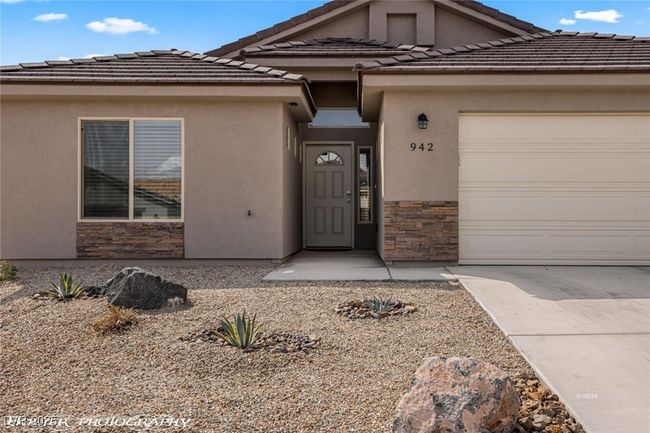 Entrance to property featuring stone siding, an attached garage, concrete driveway, and a tile roof | Image 7