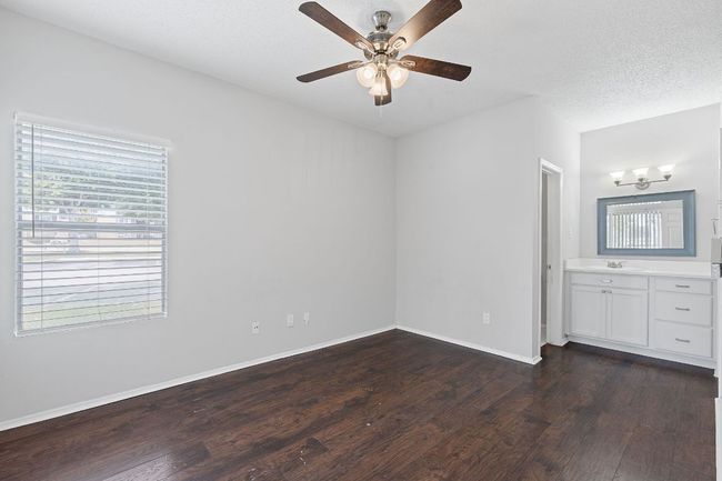 Unfurnished bedroom with multiple windows, dark wood finished floors, baseboards, and a sink | Image 12