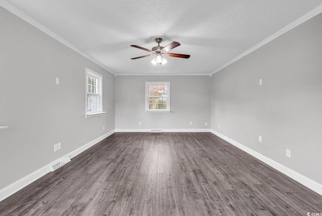 Unfurnished room with ceiling fan, healthy amount of natural light, dark wood-style floors, crown molding, and a textured ceiling | Image 5